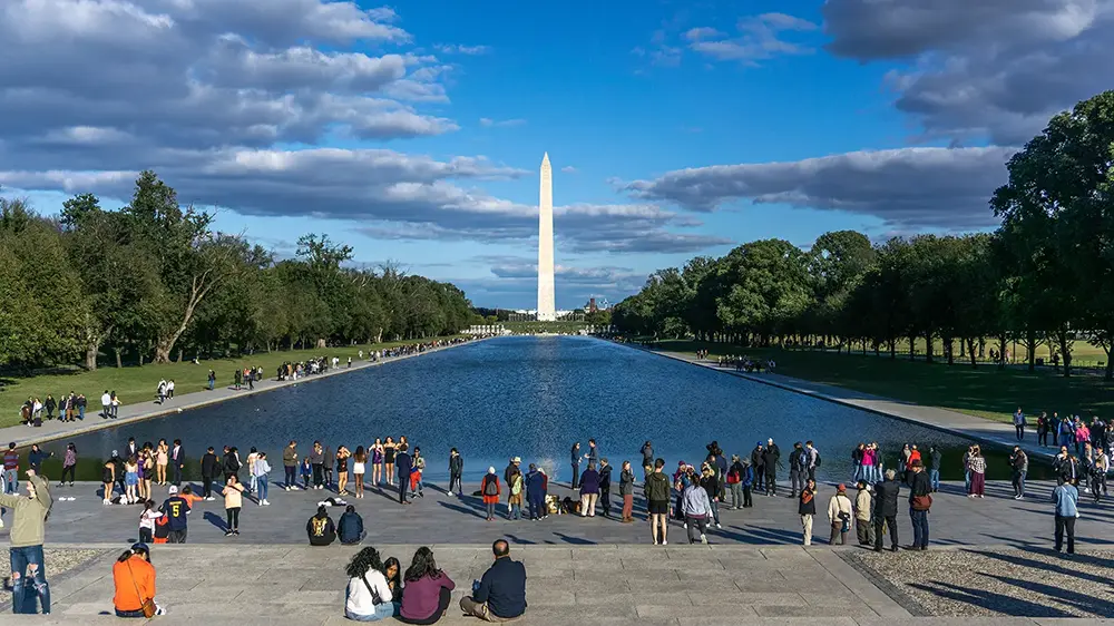 Washington Monument with the reflecting pool in front, people standing around and taking pictures.
