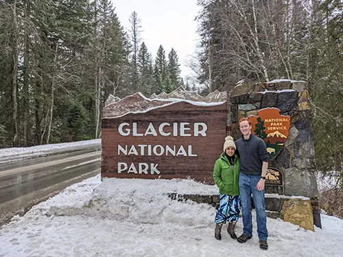 Minerva and Samuel stand in front of the Glacier National Park sign during winter - Photo taken 2021
