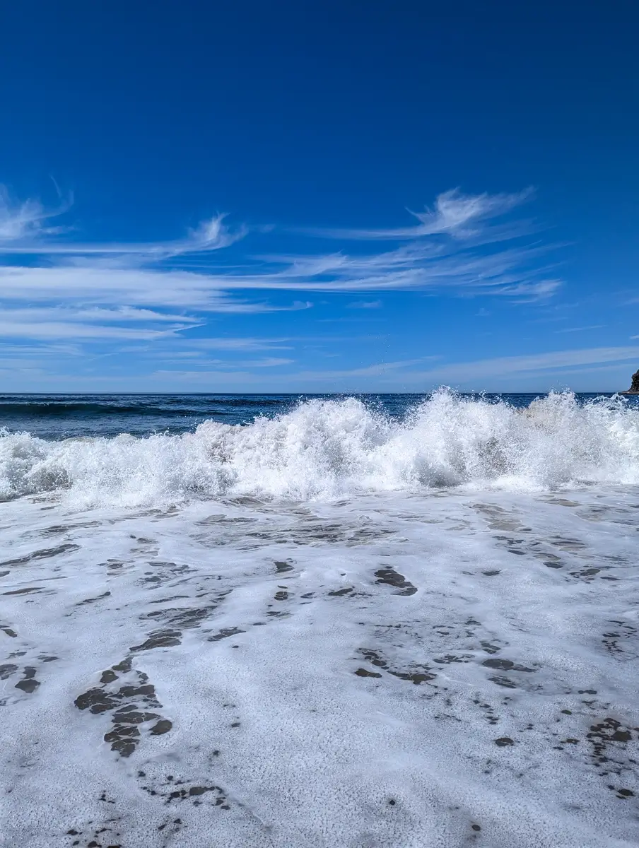 Shi Shi Beach Pacific Ocean Sam Gone Pacific Ocean waves crest along Shi Shi Beach Washington. The sky is blue and full of wispy clouds. Frothy ocean water is pushed up onto the sand.