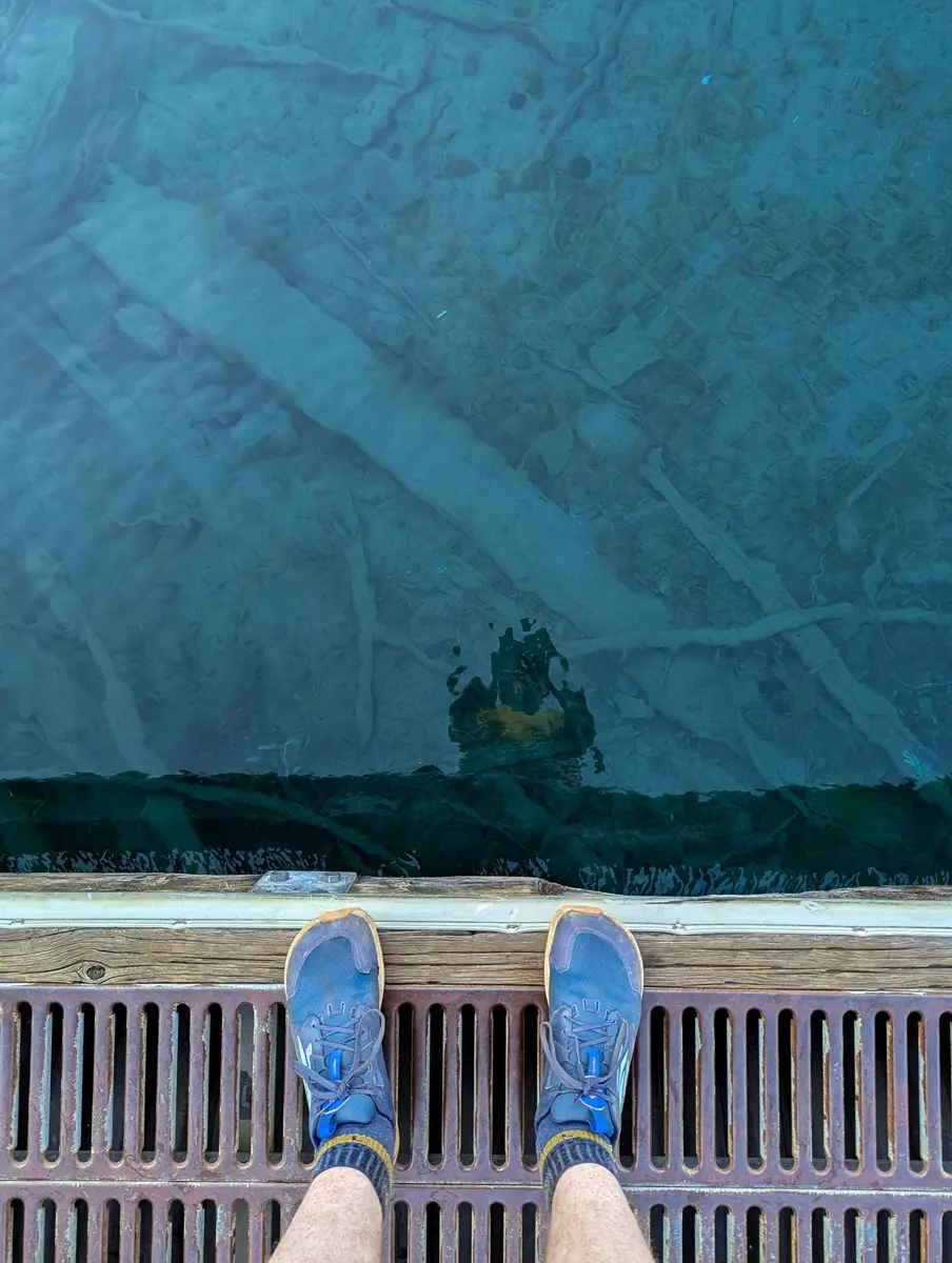Clear Water Of Lake Crescent Looking down at crystal-clear turquoise water in Lake Crescent, Washington, with submerged tree trunks and lakebed details visible beneath a dock — a peaceful stop near the Marymere Falls hike in Olympic National Park.