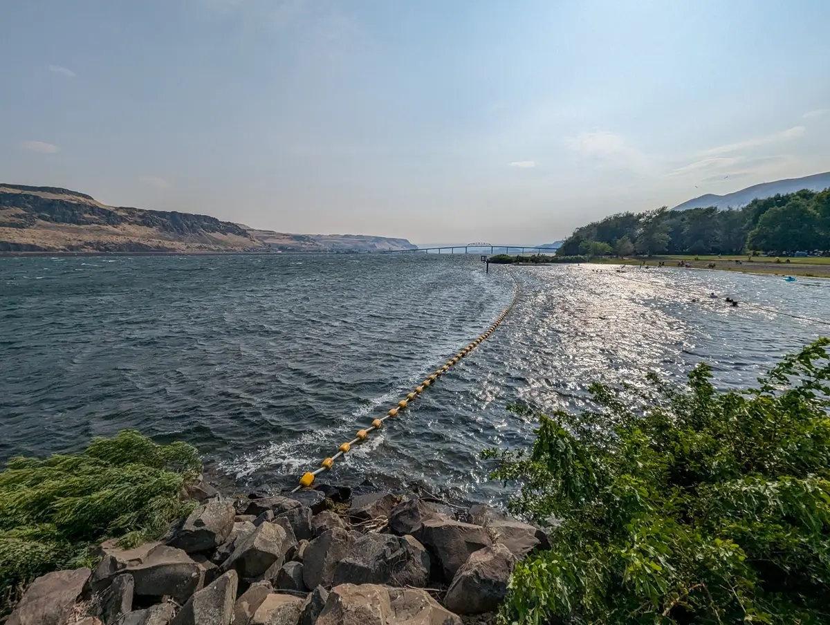 Maryhill State Park Columbia River A sweeping view of the Columbia River at Maryhill State Park shows a floating barrier curving through choppy water toward a bridge, with rocky shores and golden cliffs under a soft afternoon light.