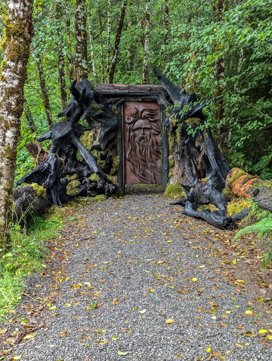 Mystical Door At Mossquatch Washington A unique, hand-carved mystical door featuring a bearded face, framed by gnarled tree roots, creates an enchanting entrance to a forest trail at Mossquatch Resort near Forks, Washington.