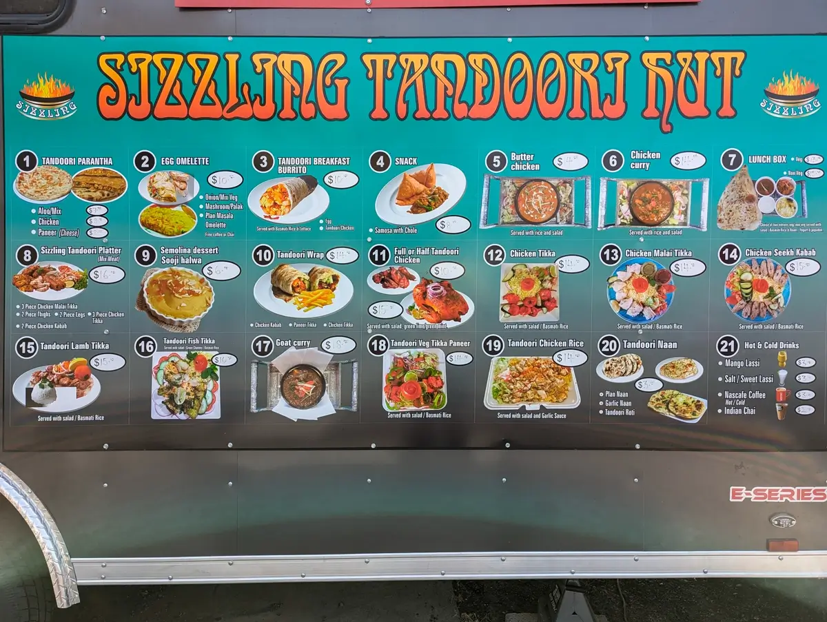 Punjabi Dhaba Menu A colorful menu on the side of the Sizzling Tandoori Hut food truck in Biggs Junction lists Indian dishes like butter chicken, tandoori wraps, samosas, lamb tikka, and mango lassi, with photos and prices next to each item.