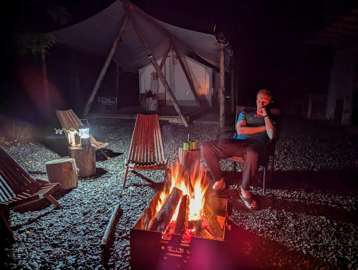 Wood Burning Fire At Mossquatch WA A cozy evening scene at Mossquatch Resort featuring a person relaxing by a warm wood-burning fire in front of a canvas glamping tent, highlighting the unique glamping experience in Olympic Peninsula.