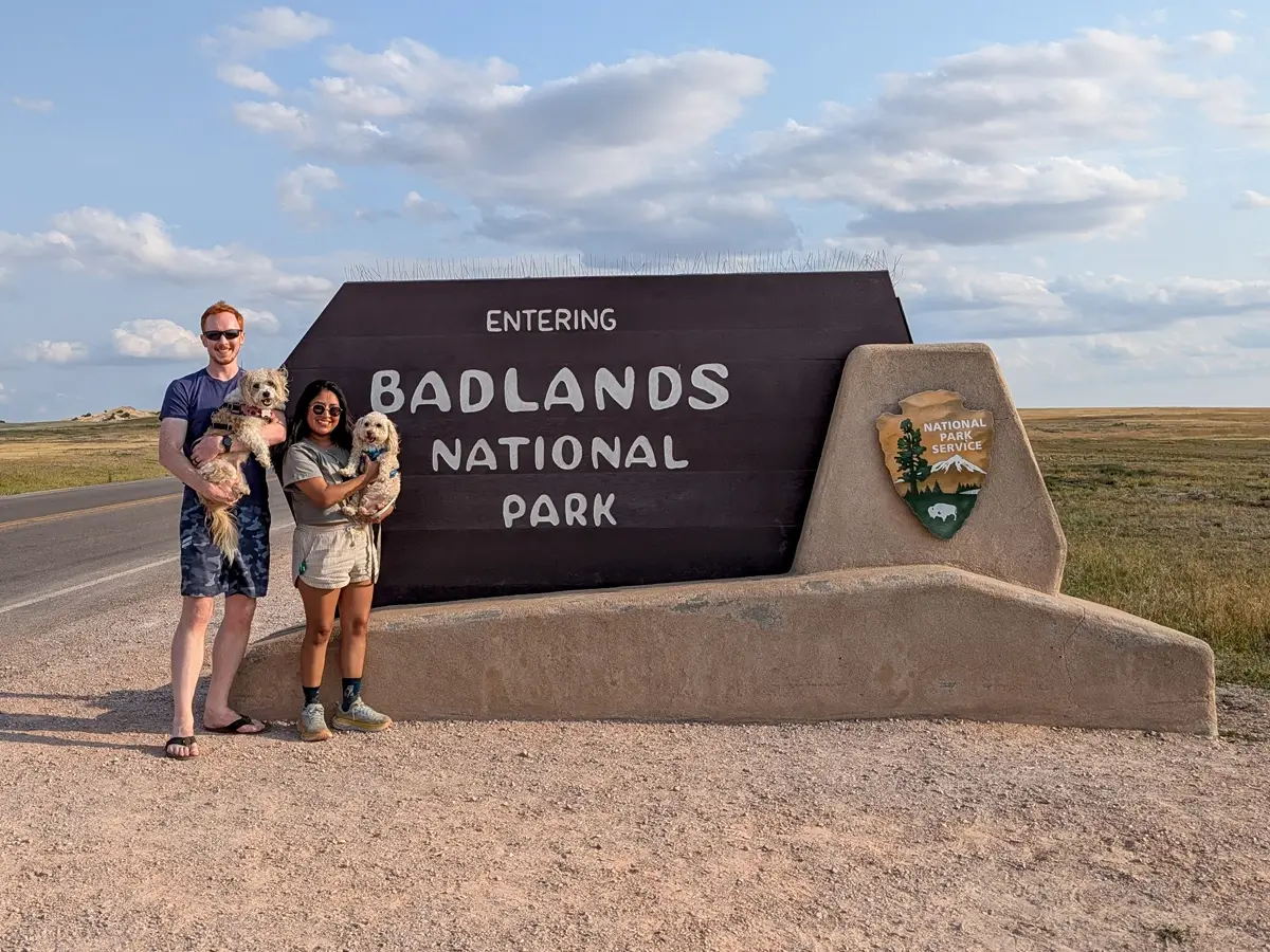 Badlands National Park Sign With Dogs Couple holding two small dogs in front of the "Entering Badlands National Park" sign in South Dakota.