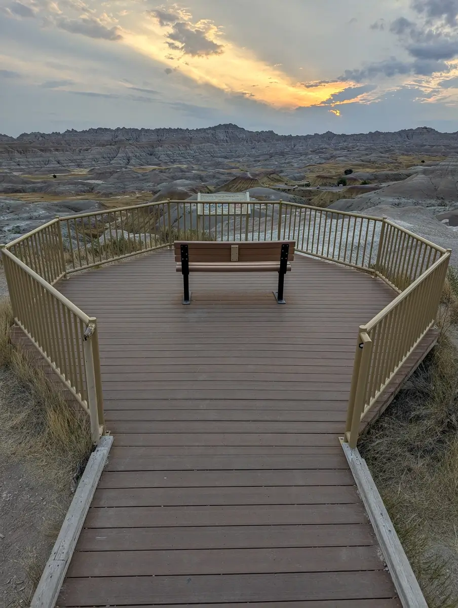 Conata Basin Overlook Bench Badlands NP Empty wooden bench on an observation deck at Conata Basin Overlook, facing the sculpted landscape of Badlands National Park at sunset.