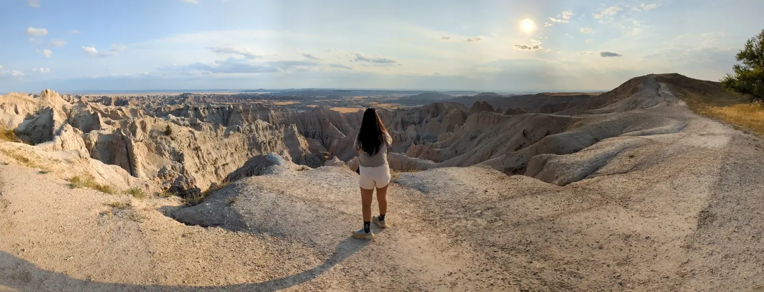 Minerva At Ancient Hunters Overlook Badlands NP Woman standing at Ancient Hunters Overlook looking out over the vast, layered formations of Badlands National Park at sunset.