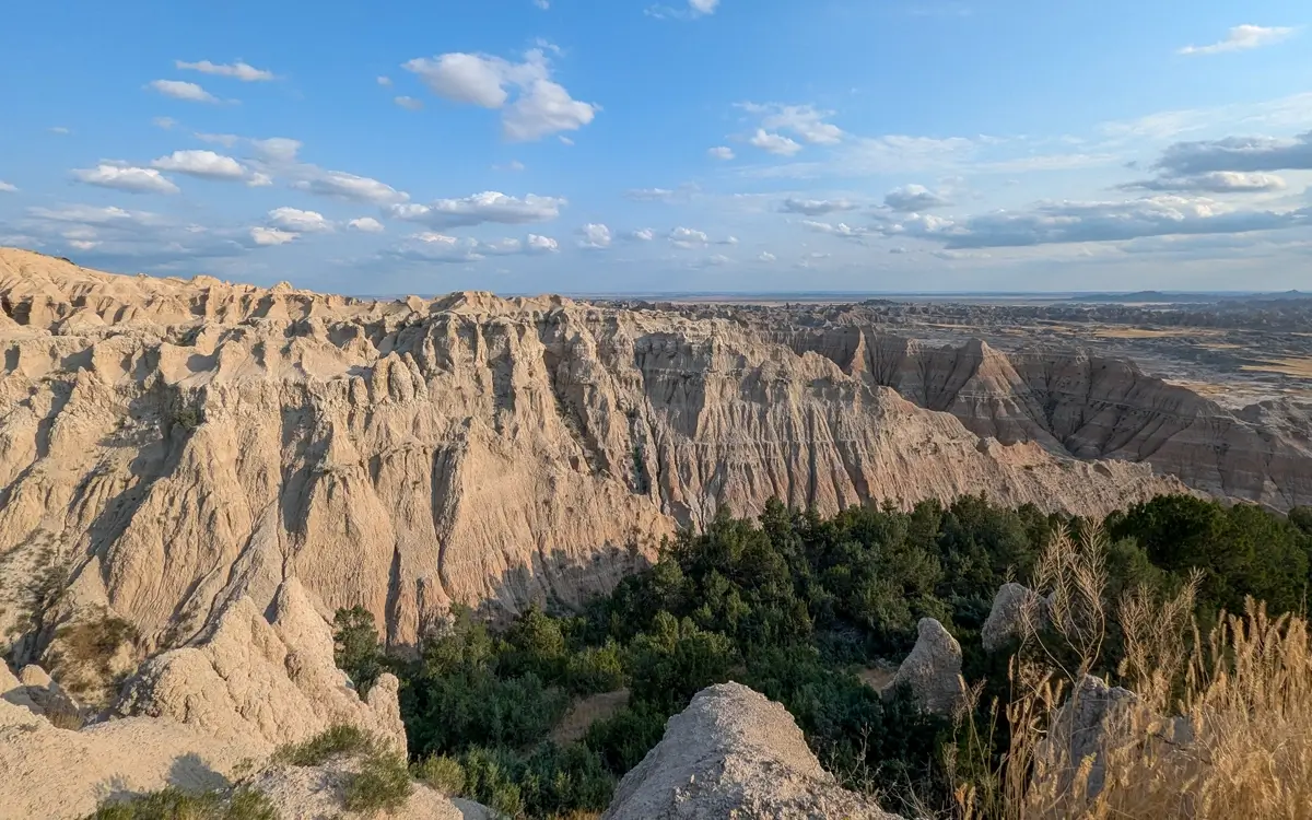 Pinnacles Overlook Badlands National Park South Dakota Scenic view of sharp, eroded Badlands rock formations and a patch of green trees and bushes in the valley below the Pinnacles Overlook.