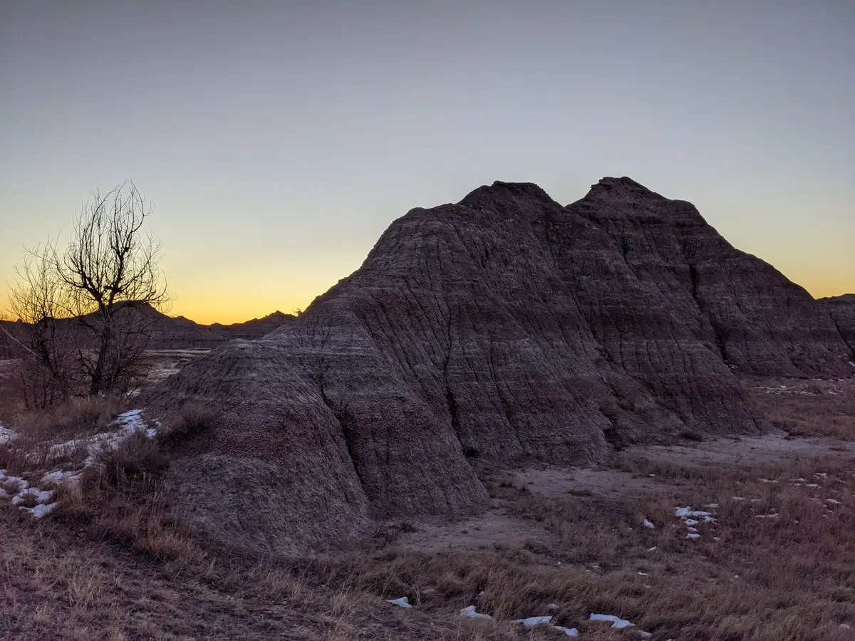 Badlands Sunrise Close-up of a dramatic rock formation silhouetted against a vibrant orange and yellow sunrise in the South Dakota Badlands during winter.