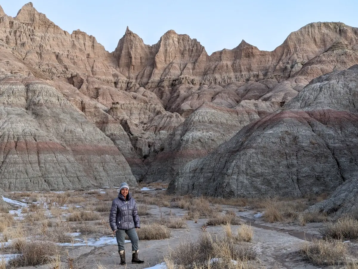 Minerva Badlands Striations A traveler standing at the base of massive grey and red sedimentary rock layers (striations) in the South Dakota Badlands during winter.