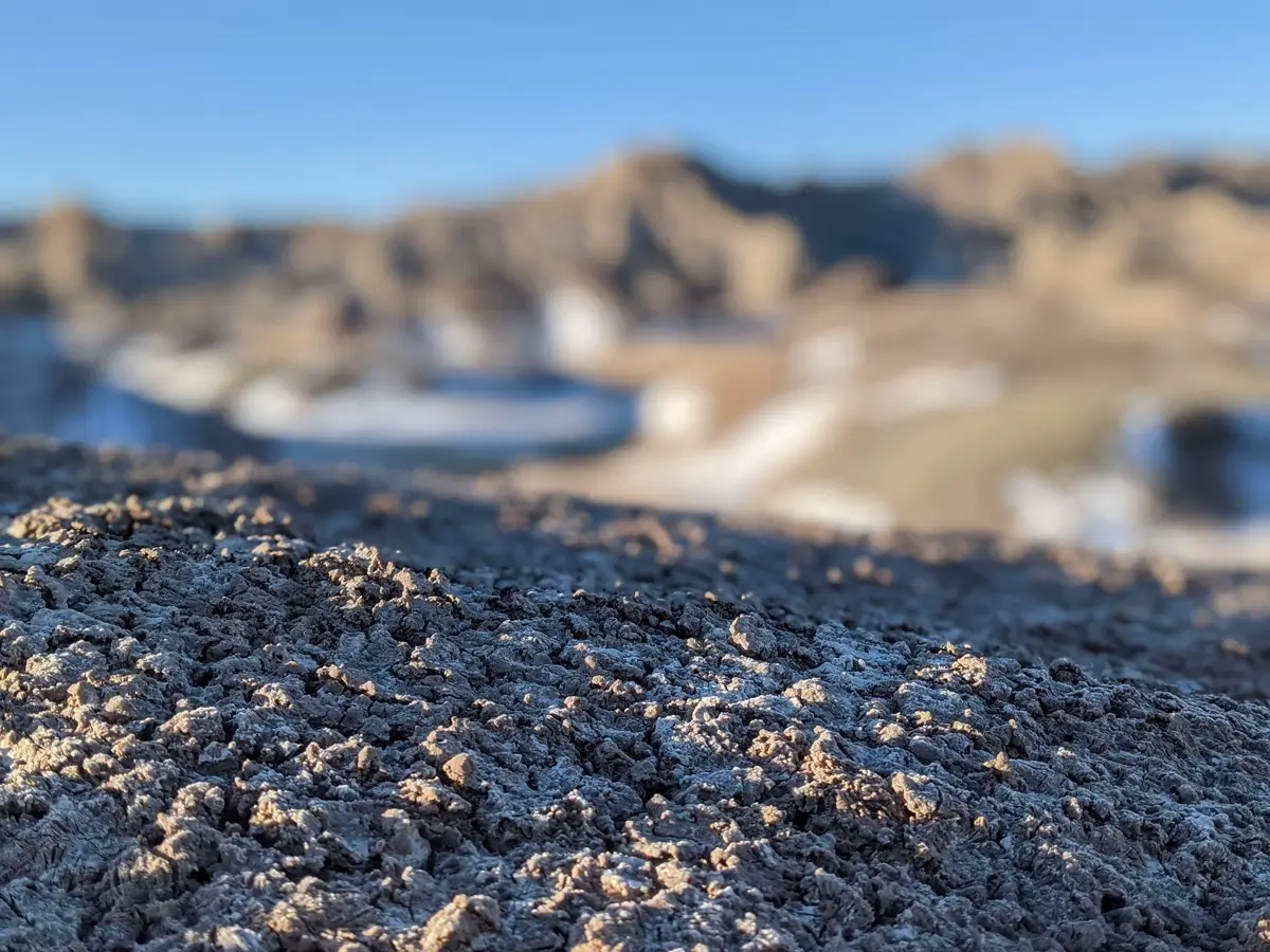 Texture Of The Badlands Winter Extreme close-up of the cracked, popcorn-textured soil of the South Dakota Badlands with frost and a blurred mountain landscape background.