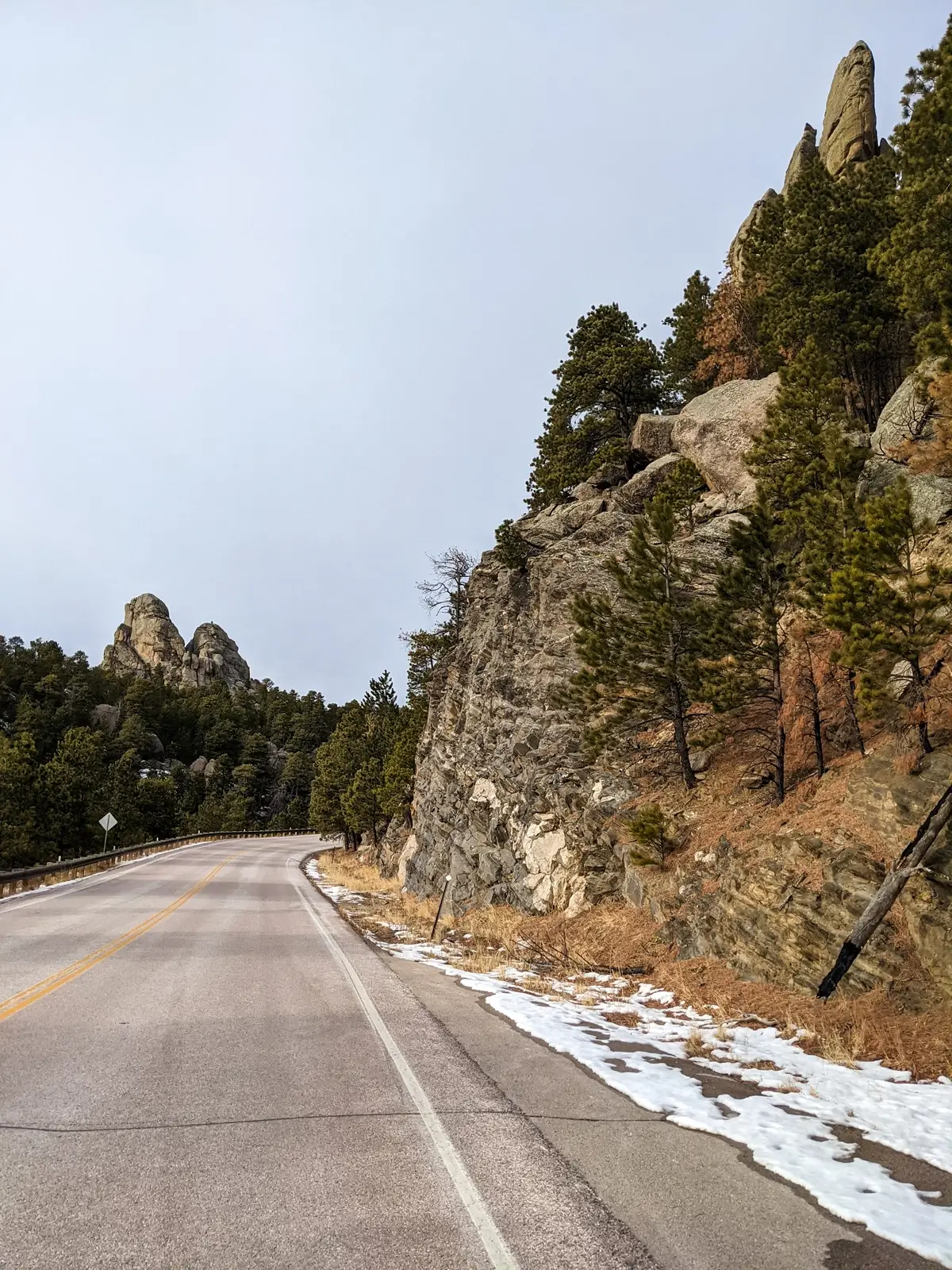 Winter drive along the paved Peter Norbeck Scenic Byway past rocky cliffs towards granite peaks near Horse Thief Lake.