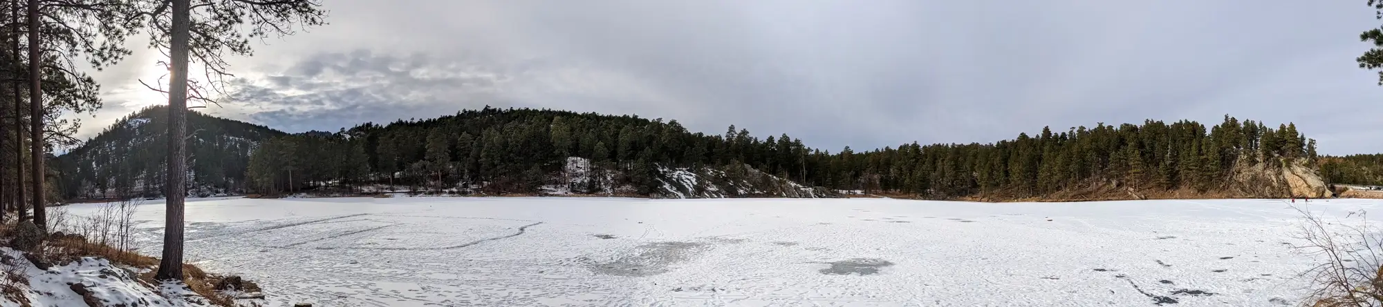 Winter panoramic view of the entirely frozen surface of Horse Thief Lake surrounded by snowy pine trees in the Black Hills of South Dakota