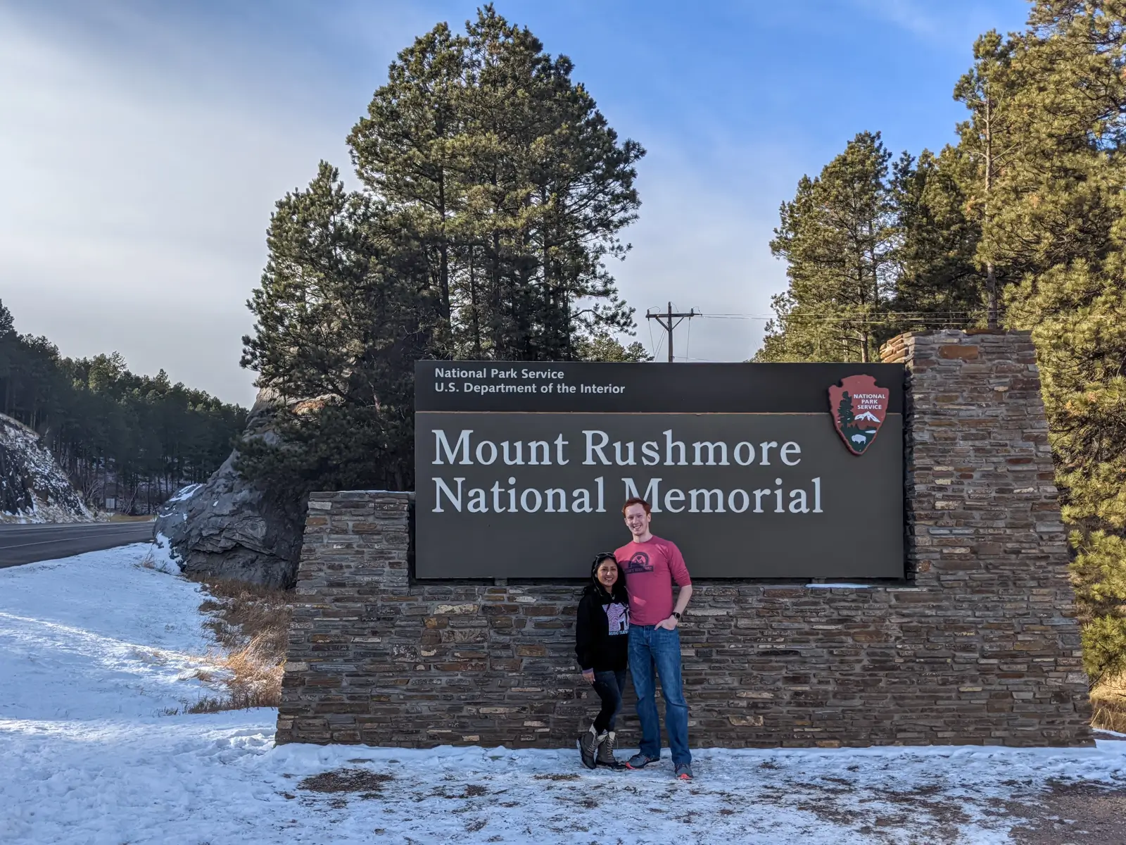 Sam and Minerva posing in front of the official brown entrance sign for Mount Rushmore National Memorial in South Dakota.