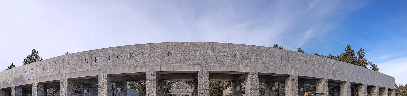 Wide view of the stone entrance archway at Mount Rushmore National Memorial in South Dakota under a blue winter sky.