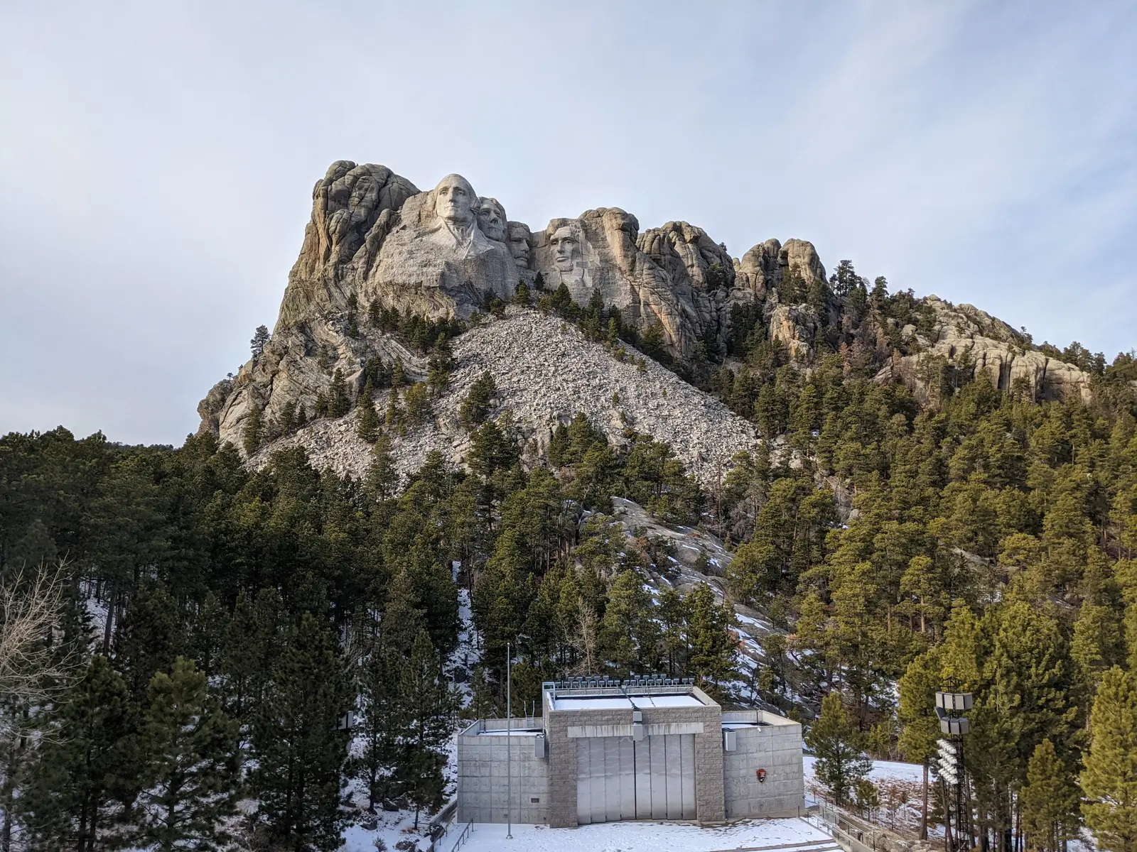 Detailed view of the four U.S. Presidents carved into Mount Rushmore with snow on the ground and pine trees in the foreground.