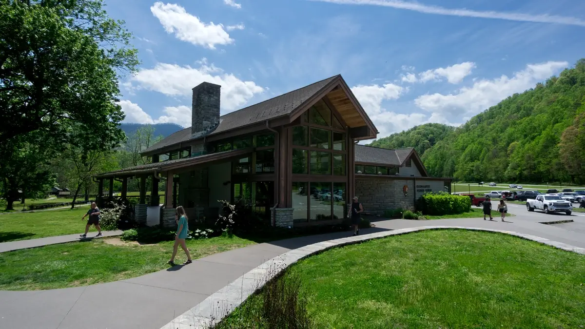 The exterior of the modern Oconaluftee Visitor Center in the Great Smoky Mountains National Park, featuring large glass windows and surrounded by green lawns and mountain views.