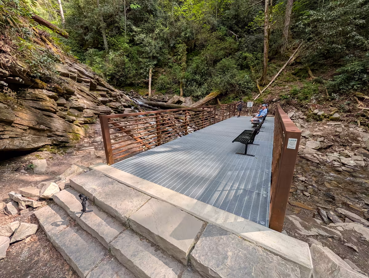 Mingo Falls Benches A metal viewing platform bridge at Mingo Falls, featuring several benches for resting, positioned over a rocky stream bed with a view of the surrounding forest.