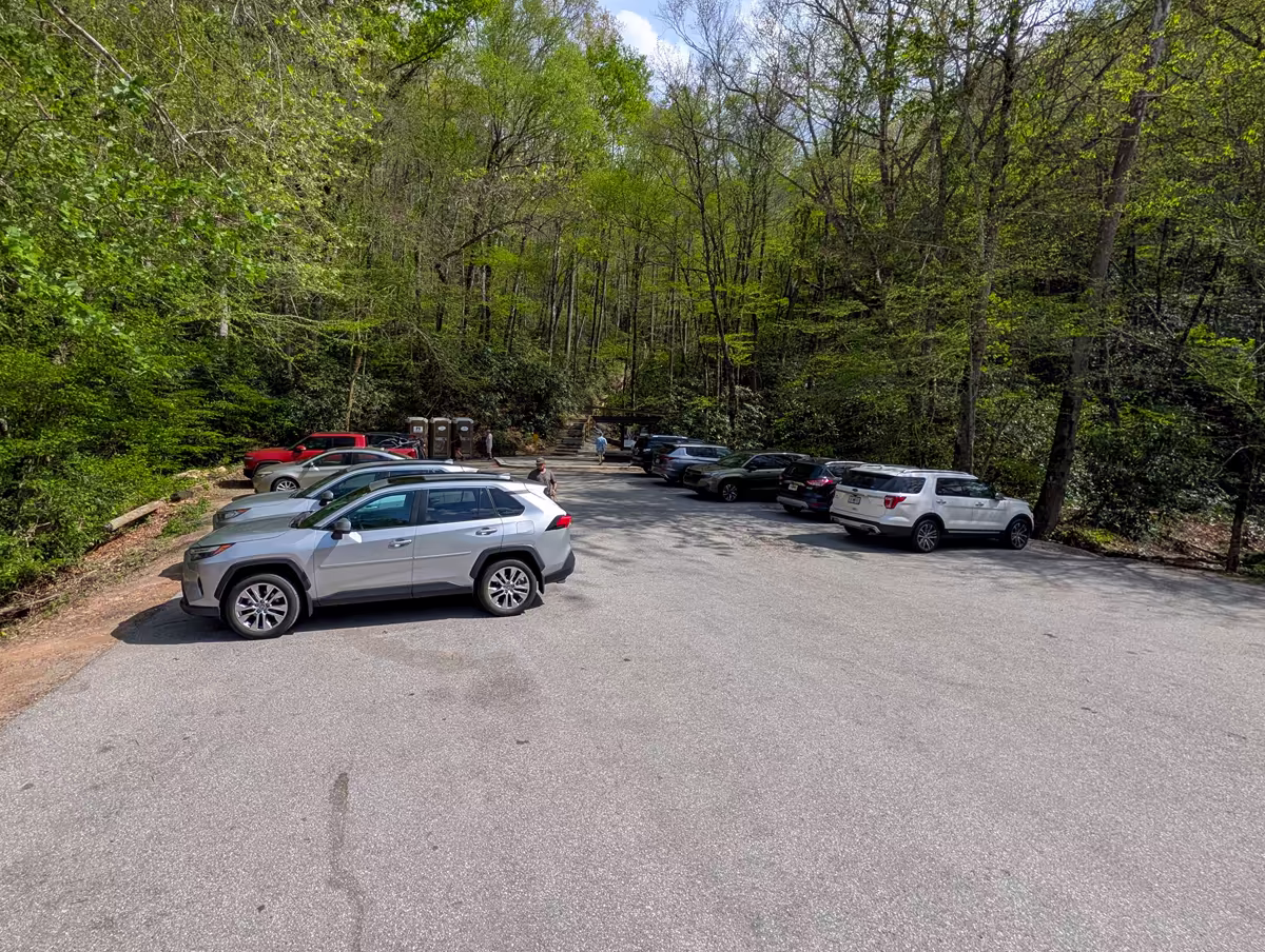Parking Lot At Mingo Falls NC The paved parking lot at the Mingo Falls trailhead with multiple vehicles parked and a view of the forest-lined path leading toward the stairs in the background.