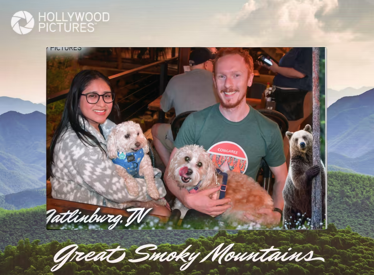 A couple smiling while dining on an outdoor patio at Howard's Restaurant in Gatlinburg, TN, holding two small, fluffy dogs, presented in a souvenir photo frame with a Smoky Mountains backdrop.